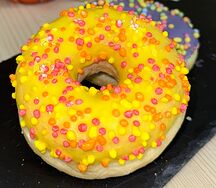 Пончик-донатс с манговой начинкой, желтой кондитерской глазурью и цветной посыпкой