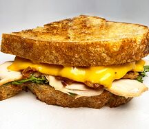 Сэндвич с индейкой, поджаренным беконом, листьями салата и сыром чеддер